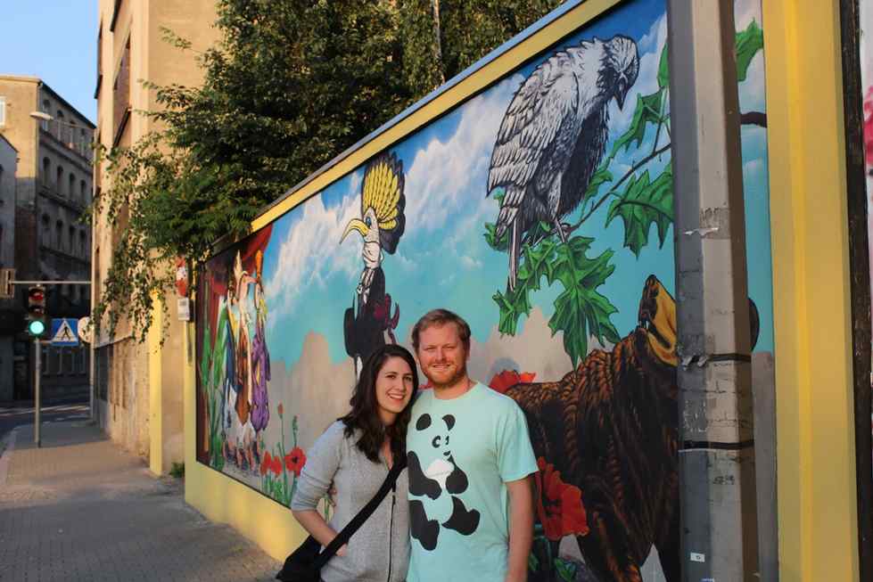Two people pose in front of colorful mural
